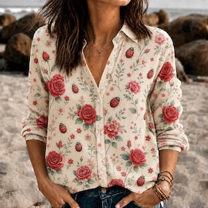 May include: A long-sleeved button-down shirt in a light beige color featuring a repeating pattern of red roses, green leaves, and small red ladybugs. The shirt has a classic collar, a front button placket, and a straight hemline design.