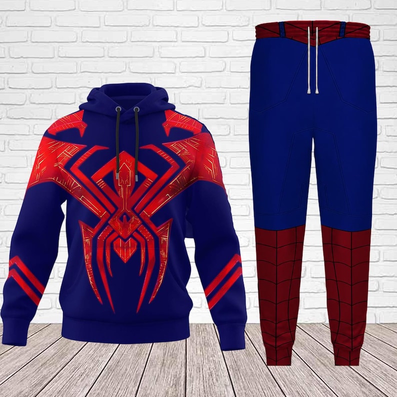 May include: A blue hoodie and matching pants set. The hoodie features a large red spider emblem on the front and shoulders. The pants are blue with red panels on the lower legs. The drawstring on the pants is white.