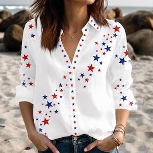 May include: A white long-sleeve button-down shirt featuring a scattered pattern of red and blue stars. The shirt has a classic collar, a central button placket, and long sleeves. The star print is concentrated along the front placket and sleeves.