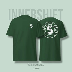 May include: A dark green t-shirt with the text "INNER SHIFT" in a light gray font. The front of the shirt has a white logo on the left chest. The back of the shirt features a circular design with the words "INNER SHIFT" and a white logo.