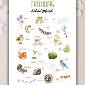 May include: A white poster with the German word "FR&Uuml;HLING" and the phrase "Schnitzeljagd" in black script. The poster features watercolor illustrations of spring-themed items like flowers, a frog, a caterpillar, and a butterfly.
