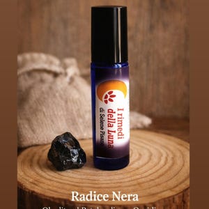 Puede incluir: Un frasco roll-on de vidrio azul con tapa negra, etiquetado "I rimedi della Luna" y "Radice Nera". Una piedra de obsidiana negra se encuentra junto al frasco sobre una rodaja de madera. El fondo es borroso, de tono neutro.