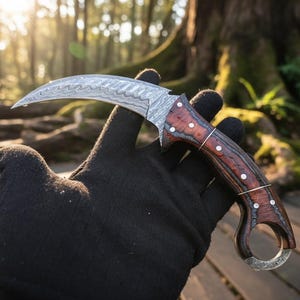 May include: A curved karambit knife with a patterned steel blade and a wooden handle. The handle features a dark wood grain with white dot accents. The knife is held in a black gloved hand against a blurred forest background.
