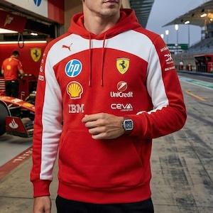 May include: Red Ferrari hoodie with white shoulder panels and a hood. The hoodie features sponsor logos including HP, Shell, IBM, and Unicredit. A Puma logo is visible on the chest. The Ferrari logo is on the chest. The hoodie has a front pocket.