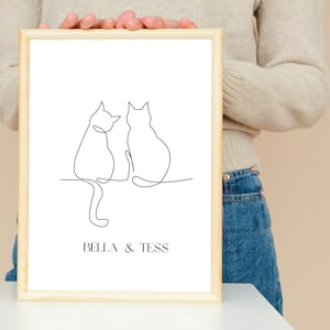 Könnte beinhalten: Ein gerahmter Strichzeichnung-Druck von zwei Katzen, die nebeneinander sitzen. Der Druck ist auf weißem Papier mit einem schwarzen Rahmen und dem Text "Bella & Tess" unten.