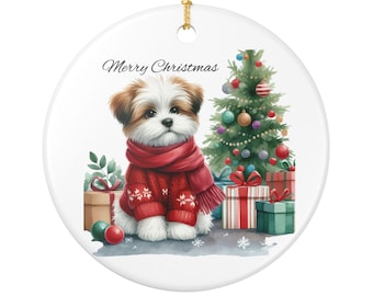 May include: A round Christmas ornament featuring a watercolor illustration of a puppy wearing a red sweater and scarf. A decorated Christmas tree and wrapped gifts are in the background. The text "Merry Christmas" is written on the ornament.