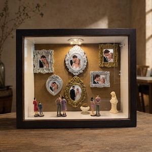 Può includere: Una bacheca in legno scuro con cinque cornici decorate nei toni dell'argento e dell'oro, ognuna contenente la fotografia di una coppia. Piccole statuette di coppie sono posizionate sulla base, insieme a un piedistallo e un vaso in miniatura.