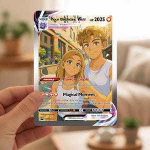 Può includere: Una carta Pokémon personalizzata con un'illustrazione di coppia, il testo "Your Birthday VMAX HP 2025" e le frasi "Power couple" e "Magical Moment". La carta è tenuta in mano, con uno sfondo sfocato.