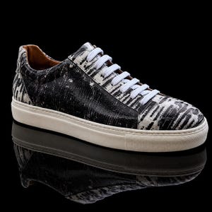 Könnte beinhalten: Ein Low-Top-Sneaker mit einem schwarz-weißen, strukturierten Muster auf dem Obermaterial. Der Schuh verfügt über weiße Schnürsenkel, ein hellbraunes Innenfutter und eine dicke, cremefarbene Gummisohle mit strukturierter Zehenkappe und glatter Basis.