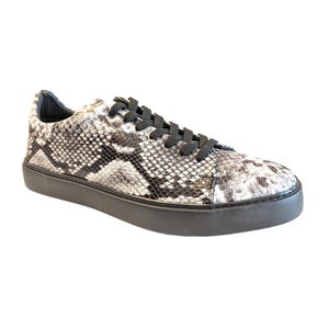 May include: A single sneaker with a snakeskin pattern in shades of gray and white. The shoe has black laces and a black sole. The sneaker is a low-top style.