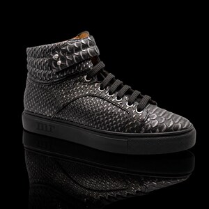 Könnte beinhalten: Ein High-Top-Sneaker mit strukturiertem schwarz-grauem Schlangenledermuster, schwarzen Schnürsenkeln und einer schwarzen Gummisohle. An der Seite der Sohle sind die Buchstaben mr eingeprägt. Der Schuh hat einen gepolsterten Schaft mit zwei silbernen Nieten.