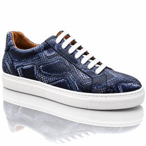 Puede incluir: Una zapatilla baja con un patrón de textura de piel de serpiente en azul oscuro y negro en la parte superior. El calzado incluye cordones blancos gruesos, una suela de goma blanca y un forro interior color canela, con un diseño estructurado.