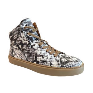 May include: High-top sneaker with a snakeskin pattern in black, white, and gray. The shoe has brown laces and a brown sole. The sneaker is made of a textured material.