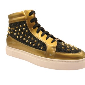 Puede incluir: Zapatillas altas doradas con detalles de charol y tejido brillante negro, adornadas con tachuelas doradas. Cordones negros y suela blanca. Calzado elegante y atrevido.