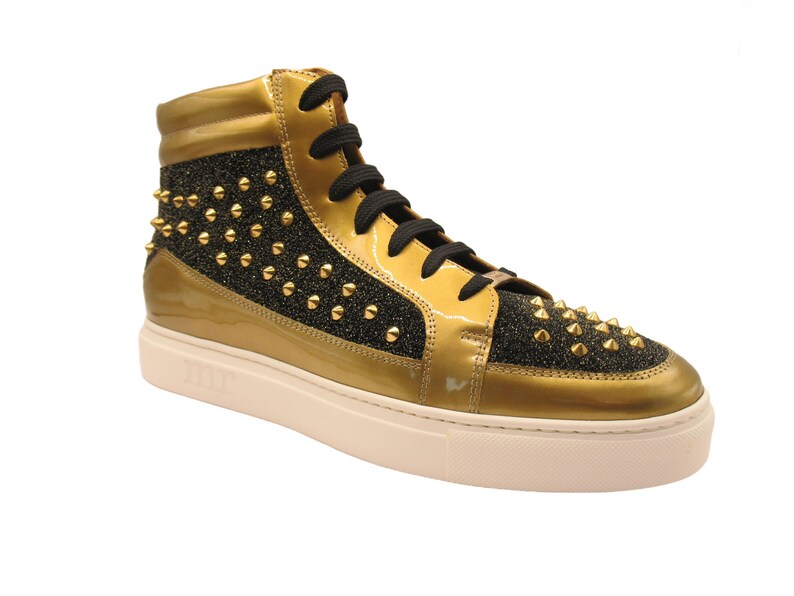 Puede incluir: Zapatillas altas doradas con detalles de charol y tejido brillante negro, adornadas con tachuelas doradas. Cordones negros y suela blanca. Calzado elegante y atrevido.