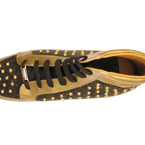 Puede incluir: Zapatilla alta dorada y negra con cordones negros. El zapato presenta detalles dorados, puntera y tal&oacute;n negros brillantes y tachuelas doradas. El interior es de color marr&oacute;n claro.