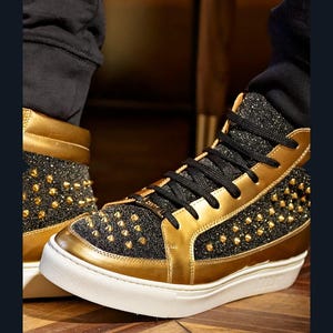 Puede incluir: Zapatillas altas con detalles dorados y negros. Los zapatos presentan ribetes dorados, una parte superior negra brillante y tachuelas doradas. Las suelas son blancas con un acento dorado. Los cordones negros completan el dise&ntilde;o.
