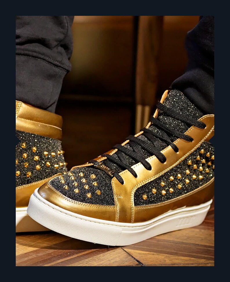 Puede incluir: Zapatillas altas con detalles dorados y negros. Los zapatos presentan ribetes dorados, una parte superior negra brillante y tachuelas doradas. Las suelas son blancas con un acento dorado. Los cordones negros completan el dise&ntilde;o.