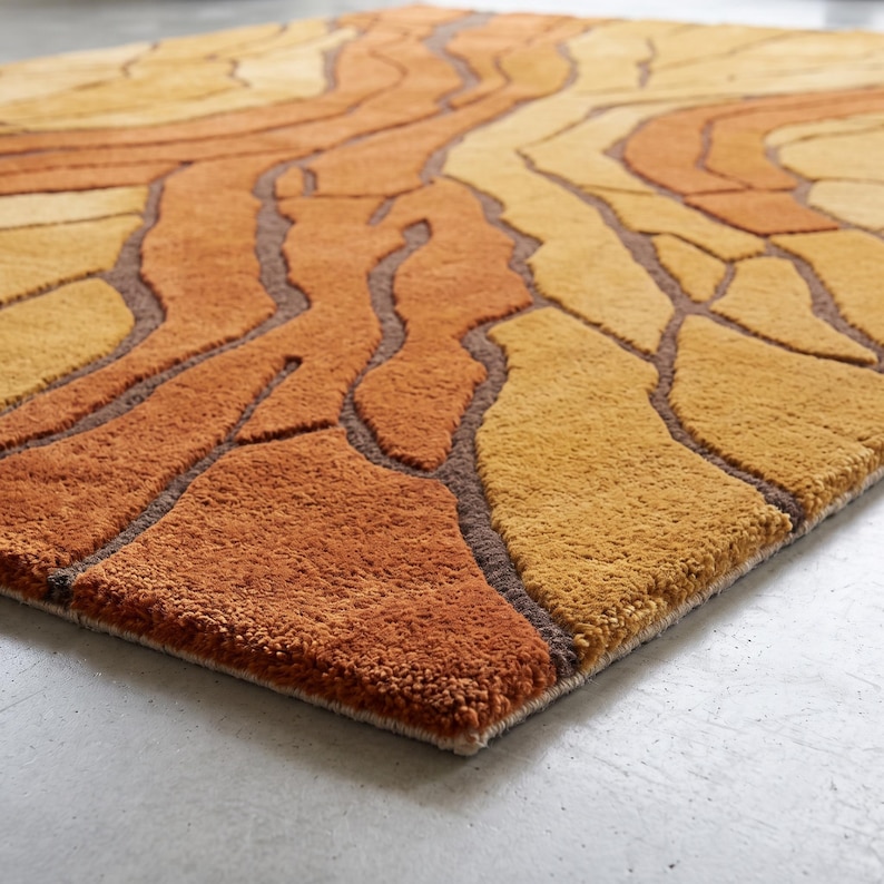 May include: A rectangular area rug featuring a textured, tufted surface with an abstract pattern of organic, flowing shapes in shades of burnt orange, golden yellow, and mustard, separated by deep brown, recessed lines that create a relief effect.