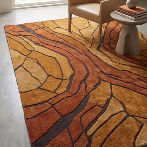 May include: A rectangular area rug featuring an abstract pattern of organic, flowing shapes in shades of burnt orange, mustard yellow, and deep brown. The design consists of raised, textured sections separated by recessed dark brown lines.