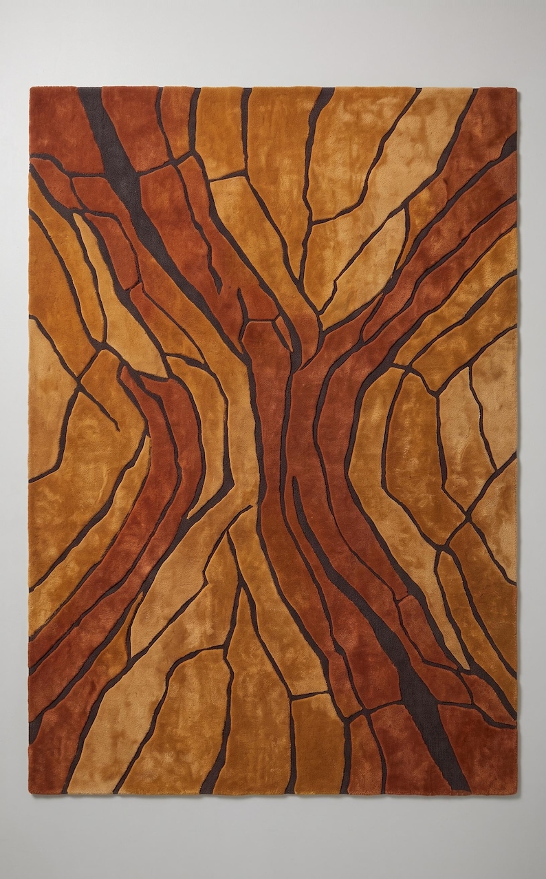 May include: A rectangular area rug featuring a textured, abstract pattern of interlocking shapes in shades of burnt orange, golden yellow, and deep brown. The design is defined by dark, recessed lines that create a cracked or fragmented appearance.