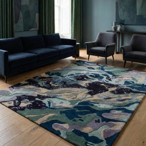 May include: A large area rug with an abstract design in shades of blue, green, and purple. The rug is placed on a hardwood floor in a living room setting. A navy blue sofa and two gray armchairs are also visible.