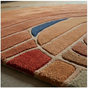 May include: Close-up of a colorful area rug with a geometric design. The rug features a pattern of rectangles and curved shapes in shades of orange, brown, red, and blue. The rug is made of a soft, textured material.