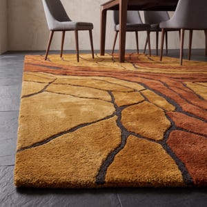 May include: A rectangular area rug featuring a textured, multi-tonal pattern of interlocking organic shapes in shades of golden yellow, burnt orange, and deep brown. The rug has a thick, plush pile and is positioned on a dark gray tiled floor.