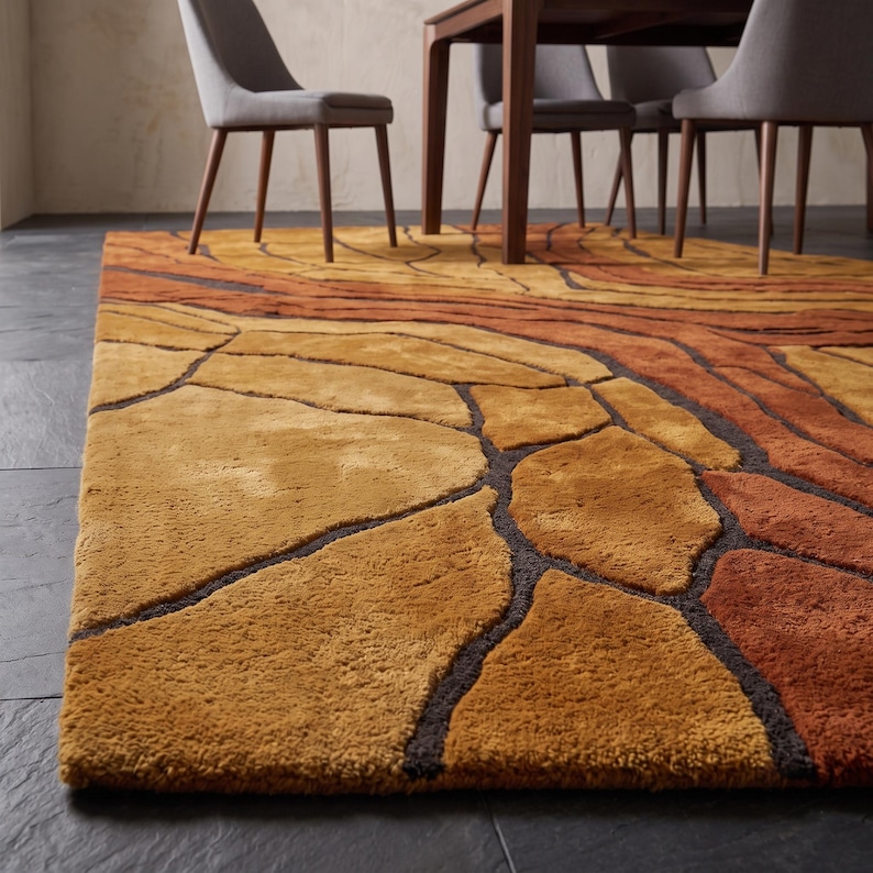 May include: A rectangular area rug featuring a textured, multi-tonal pattern of interlocking organic shapes in shades of golden yellow, burnt orange, and deep brown. The rug has a thick, plush pile and is positioned on a dark gray tiled floor.