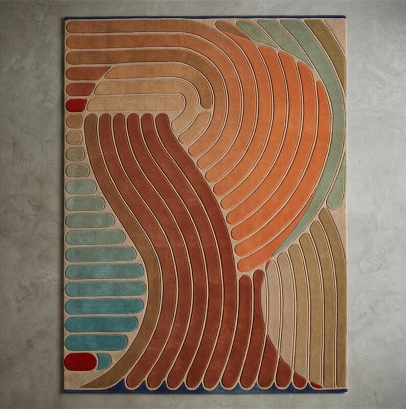 May include: A rectangular area rug with an abstract design. The rug features curved, parallel lines in shades of orange, brown, beige, and teal. A red accent is at the top left corner. The rug has a dark blue border.