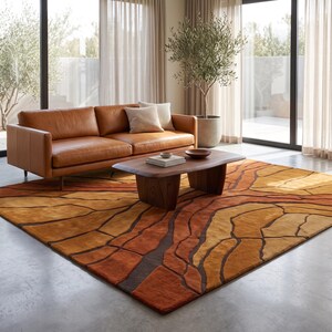 May include: A large rectangular area rug featuring a textured, abstract pattern of organic, cracked earth shapes in shades of burnt orange, mustard yellow, and deep brown, laid out on a smooth concrete floor beneath a leather sofa and coffee table.