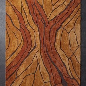 May include: A rectangular area rug featuring a textured, abstract pattern of interlocking shapes in shades of burnt orange, golden yellow, and tan, separated by deep brown recessed lines that create a dimensional, cracked earth appearance.