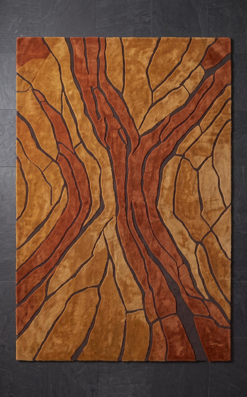 May include: A rectangular area rug featuring a textured, abstract pattern of interlocking shapes in shades of burnt orange, golden yellow, and tan, separated by deep brown recessed lines that create a dimensional, cracked earth appearance.