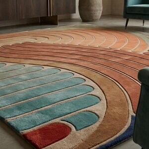 May include: A large, colorful area rug with a wave-like design. The rug features a blend of warm and cool tones, including shades of orange, brown, blue, and teal. The rug is placed on a light-colored floor, with teal armchairs in the foreground.