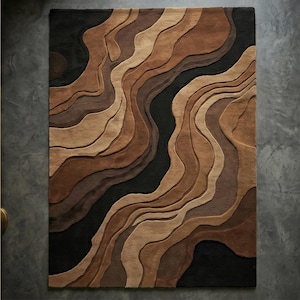 May include: A rectangular area rug with a layered, topographic design. The rug features a palette of browns, tans, and black, creating a sense of depth and dimension. The wavy lines and varied textures suggest a landscape or geological formation.