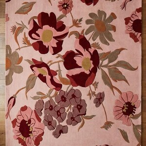 K&ouml;nnte beinhalten: Ein rechteckiger Teppich mit floralem Muster. Der Teppich zeigt gro&szlig;e, stilisierte Blumen in Burgunder-, Rosa- und ged&auml;mpften Gr&uuml;nt&ouml;nen vor einem hellrosa Hintergrund. Die Blumen haben gelbe Zentren und sind in einem dichten, sich wiederholenden Muster angeordnet.