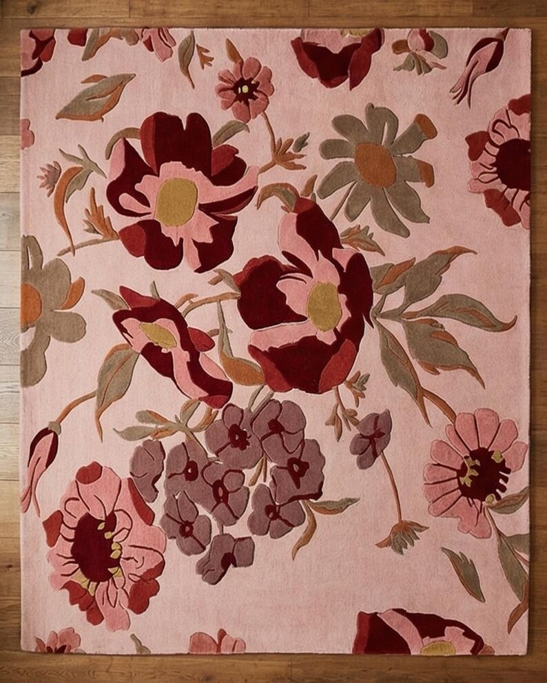 K&ouml;nnte beinhalten: Ein rechteckiger Teppich mit floralem Muster. Der Teppich zeigt gro&szlig;e, stilisierte Blumen in Burgunder-, Rosa- und ged&auml;mpften Gr&uuml;nt&ouml;nen vor einem hellrosa Hintergrund. Die Blumen haben gelbe Zentren und sind in einem dichten, sich wiederholenden Muster angeordnet.
