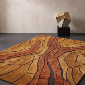 May include: A rectangular area rug featuring an abstract pattern of organic, flowing shapes in shades of burnt orange, golden yellow, and deep brown. The design consists of raised, textured sections separated by recessed dark brown lines.
