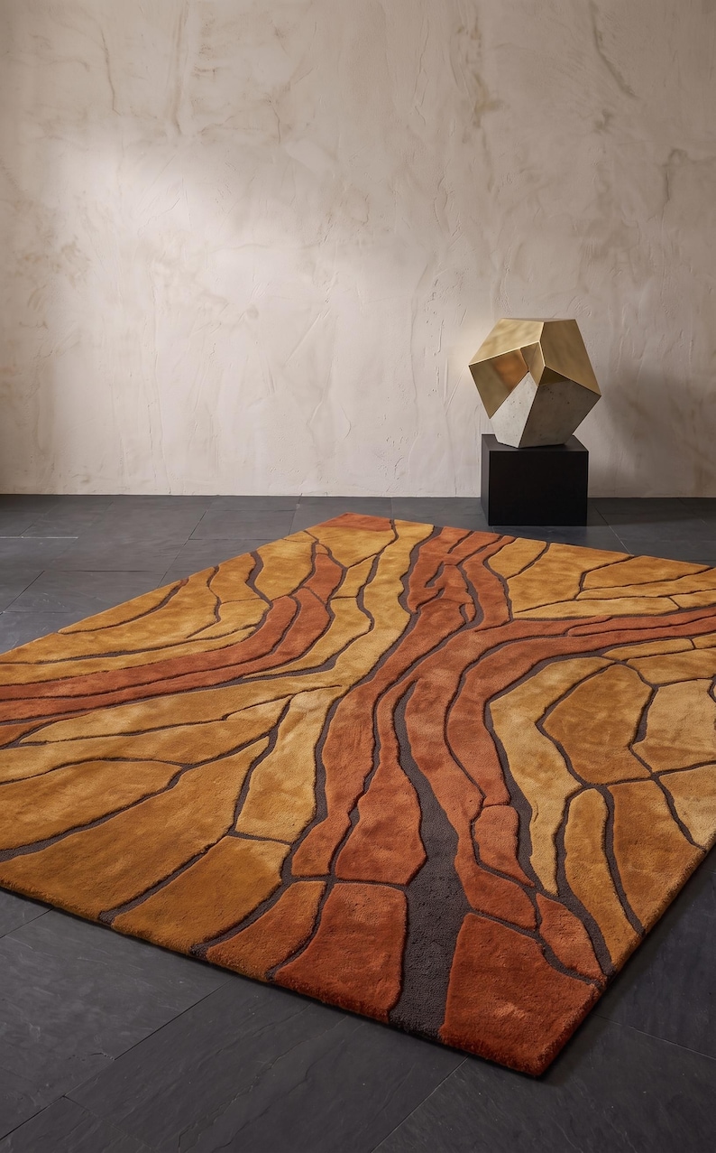 May include: A rectangular area rug featuring an abstract pattern of organic, flowing shapes in shades of burnt orange, golden yellow, and deep brown. The design consists of raised, textured sections separated by recessed dark brown lines.