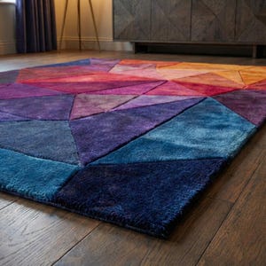 K&ouml;nnte beinhalten: Ein farbenfroher geometrischer Teppich mit einem Farbverlauf von Blau-, Lila-, Rot-, Orange- und Gelbt&ouml;nen. Der Teppich besteht aus einem weichen, pl&uuml;schigen Material und weist ein modernes, abstraktes Design auf. Der Teppich ist rechteckig.