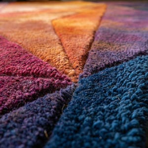 K&ouml;nnte beinhalten: Nahaufnahme eines farbenfrohen Teppichs mit geometrischem Design. Der Teppich weist einen Farbverlauf auf, darunter tiefes Rot, Orange, Lila und Blau. Die Textur erscheint weich und pl&uuml;schig, mit sichtbaren Schlaufen.