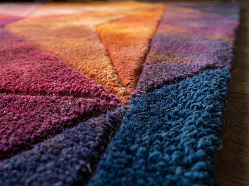 K&ouml;nnte beinhalten: Nahaufnahme eines farbenfrohen Teppichs mit geometrischem Design. Der Teppich weist einen Farbverlauf auf, darunter tiefes Rot, Orange, Lila und Blau. Die Textur erscheint weich und pl&uuml;schig, mit sichtbaren Schlaufen.