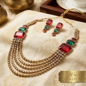 May include: A multi-strand gold-toned necklace and matching earring set featuring rectangular red and green faceted stones. The necklace has five layered chains with textured gold beads and a gold plaque reading Wacy's COLLECTION.