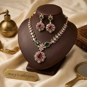 May include: A necklace and earring set featuring teardrop-shaped red and green stones surrounded by small clear crystals in a metallic setting. The necklace has a central pendant and leaf-like links. A gold-toned plaque reads wacy's collection.