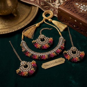 May include: A gold-toned jewelry set featuring a necklace with a drawstring tassel, a maang tikka, and two matching earrings. Each piece is adorned with clusters of small, multicolored beads in pink, orange, and green, accented by clear stones. Wacy's Collection.