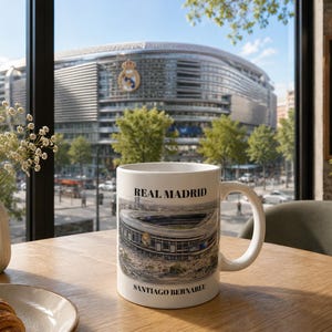 Pu&ograve; includere: Una tazza in ceramica bianca con una stampa grafica dello stadio Santiago Bernab&eacute;u. Il testo "REAL MADRID" &egrave; stampato in nero sopra l'immagine dello stadio, e "SANTIAGO BERNABEU" &egrave; stampato in nero sotto l'immagine sulla tazza.