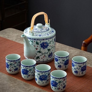 Puede incluir: Juego de té de cerámica con una tetera y seis tazas a juego. La tetera es de color azul claro con un diseño floral en azul y blanco y un asa de bambú. Las tazas tienen un patrón floral similar.