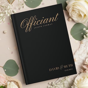 Pode incluir: Um livro de visitas de casamento preto com letras douradas. A palavra "Officiant" está escrita em um script elegante no topo, com "Joseph Conway" abaixo. Os nomes "David & Ruth" e a data estão na parte inferior.
