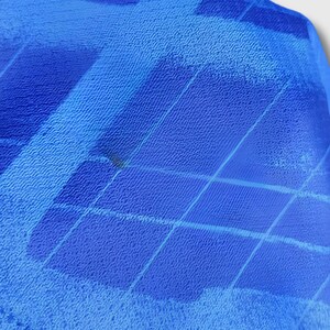 Puede incluir: Primer plano de una tela azul con superficie texturizada. La tela tiene un patr&oacute;n de formas diagonales y rectangulares en diferentes tonos de azul. La tela parece estar doblada o drapeada, con una ligera sombra visible.