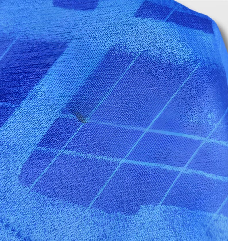 Puede incluir: Primer plano de una tela azul con superficie texturizada. La tela tiene un patr&oacute;n de formas diagonales y rectangulares en diferentes tonos de azul. La tela parece estar doblada o drapeada, con una ligera sombra visible.